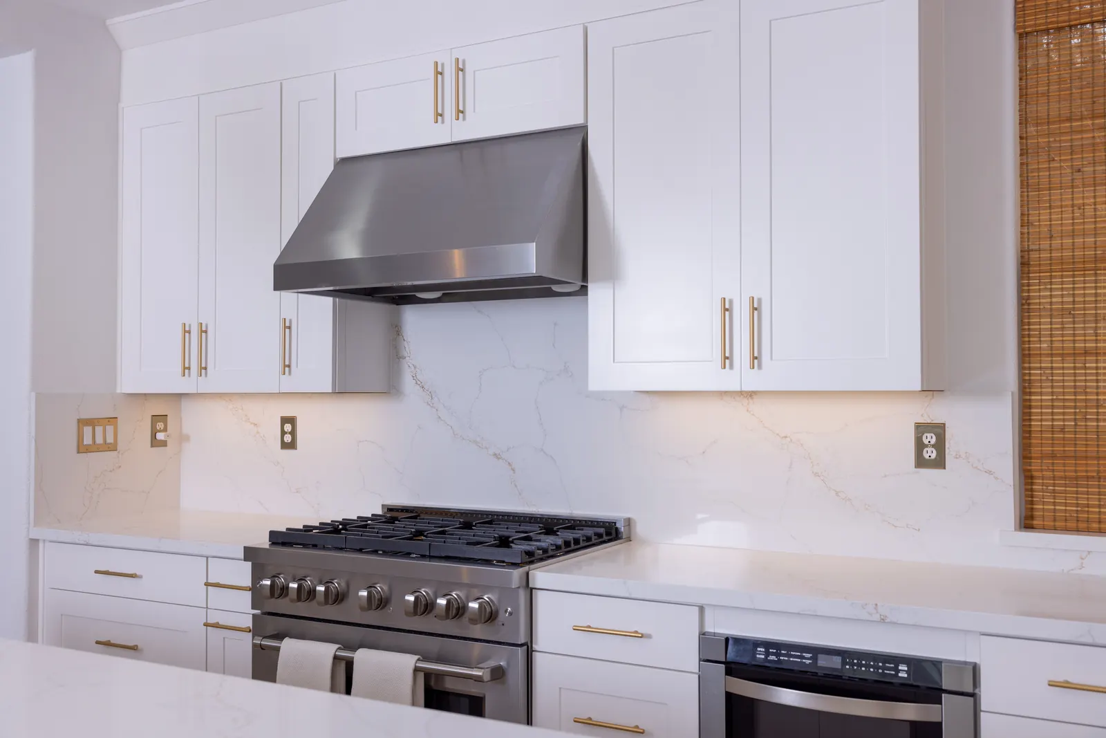 White cabinets with stainless range hood and quartz backsplash