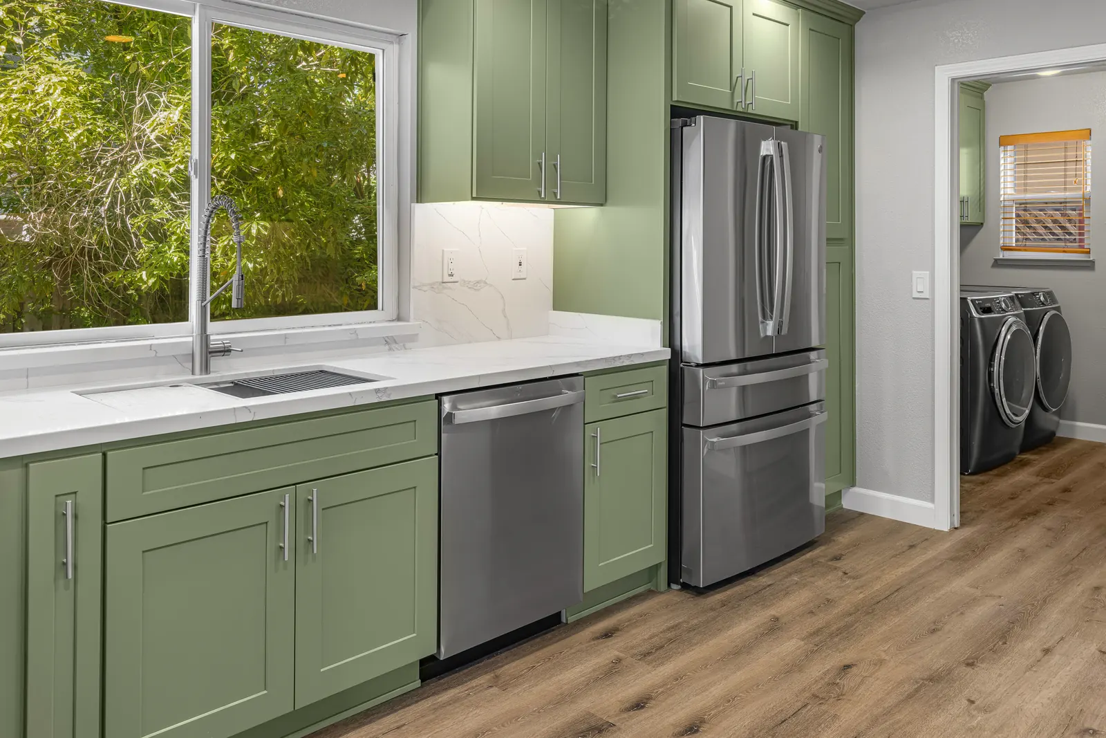Green kitchen cabinets with stainless appliances and sink window